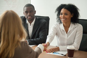 two smiling people.  one is shaking hands with a third person.